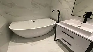 Modern bathroom in Altrincham featuring a freestanding white bathtub, black faucet, and a sleek white vanity with black accents.