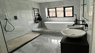 Modern, spa-like marble bathroom in Liverpool featuring a freestanding tub, black fixtures, double vessel sinks, and a walk-in shower.