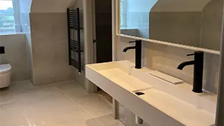 Contemporary bathroom in Lymm featuring a double-sink vanity with black faucets, neutral-toned tiles, and a black heated towel rail.