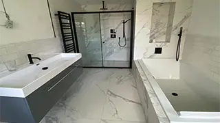 Contemporary marble-effect bathroom in Huyton featuring a walk-in shower with black-framed glass, modern bathtub, and a sleek double vanity.