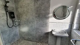 Modern bathroom in Warrington featuring a walk-in shower with textured gray panels, a round mirror, and a classic white sink.